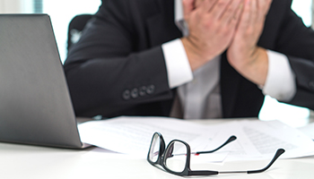 A stressed man sitting at a desk, looking overwhelmed by paperwork